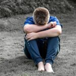 思春期の男の子がしゃがみこんで一人で悩んでいる