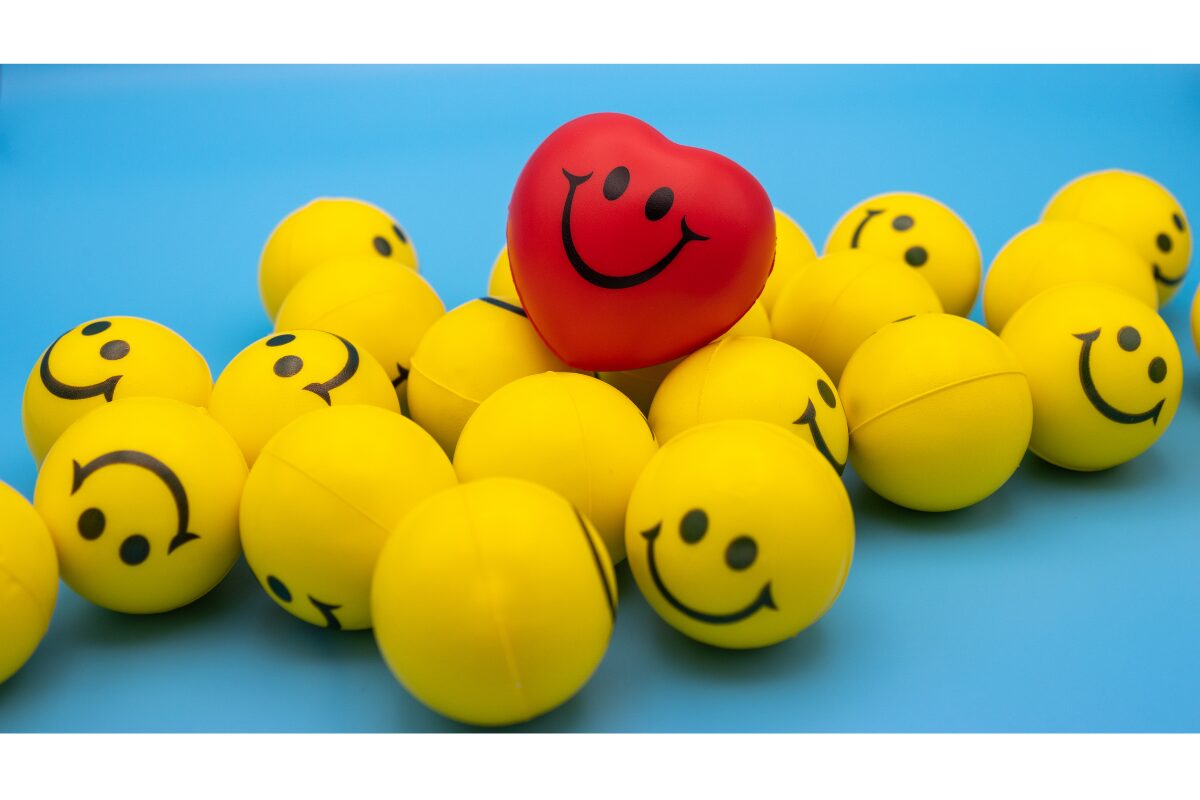 スマイルが描かれた黄色い沢山のボール。その上に赤いハート型のスマイルが1つ乗って、運ばれていく。