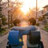 ２人の小学生が肩を組んで夕日に向かって帰るところ